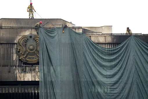 Municipal workers cover the burnt city hall building for repairing in Almaty, Kazakhstan, Thursday, Jan. 13, 2022. President Kassym-Jomart Tokayev has blamed the unrest on foreign-backed «terrorists» and requested assistance from the Collective Security Treaty Organization, a Russia-led military alliance of six ex-Soviet states. The bloc sent over 2,000 troops to Kazakhstan last week. On Tuesday Tokayev declared their mission complete and said they would start pulling out on Thursday. (AP Photo/Sergei Grits)