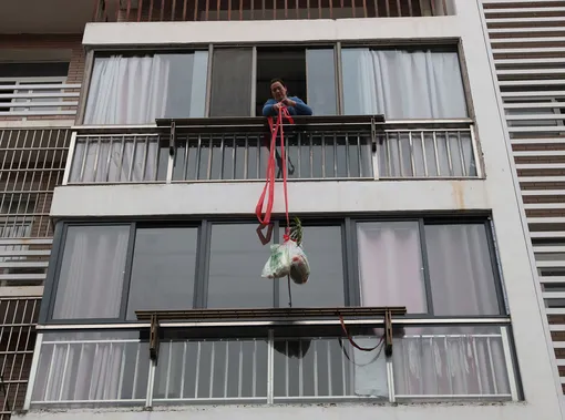 Житель города Ичан в китайской провинции Хубэй поднимает на веревке продукты, доставленные социальными службами. Жилой комплекс, в котором живет мужчина, был помещен на жесткий карантин по коронавирусу. Снимок сделан 22 февраля 2020