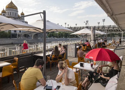People enjoy warm sunset at an outdoor terrace at an embankment of the Moscow River with the Christ the Savior Cathedral in the background in Moscow, Russia, Tuesday, June 16, 2020. Outdoor spaces in cafes and restaurants, museums and zoos have reopened in Russia's capital on Tuesday as part of easing the coronavirus restrictions. (AP Photo/Alexander Zemlianichenko)