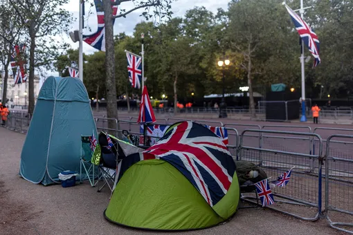 Человек спит рядом с палаткой, покрытой британским флагом, когда люди разбивают лагерь в торговом центре перед государственными похоронами британской королевы Елизаветы в Лондоне, Великобритания, 18 сентября 2022 года.