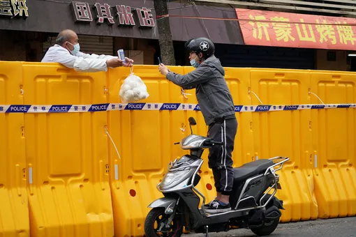 A man standing on a scooter scans a QR code to buy food from a vendor behind barricades of a sealed-off area, following the coronavirus disease (COVID-19) outbreak in Shanghai, China March 30, 2022. REUTERS/Aly Song