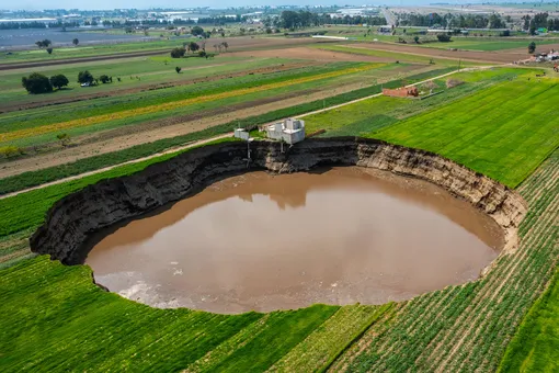 Giant Sinkhole Threatens A House And Sown Fields in PueblaSANTA MARIA ZACATEPEC, MEXICO — JUNE 09: Aerial view of a giant sinkhole on June 09, 2021 in Santa María Zacatepec, Mexico. The giant sinkhole is located 20 kilometers northwest from the capital city Puebla, the hole now measures 110 meters across its widest point, covering around 11,000 square meters and damaging a house built near the place where it appeared. Farmers of the surroundings have been affected since they are not allowed to enter their fields due to the warning perimeter set up by the authorities. (Photo by Hector Vivas / Getty Images)