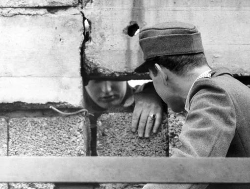 Полицейский из Западного Берлина (справа) разговаривает с жителем Восточного Берлина (слева) через дыру в Берлинской стене 19 сентября 1962 года.
