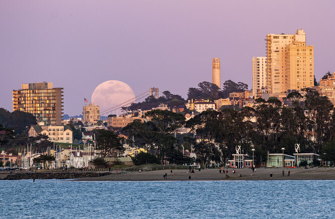 Розовая Луна поднимается над горизонтом, пока люди наслаждаются свежим воздухом на пляже. При этом по всей стране объявлен карантин по коронавирусу и режим самоизоляции. Сан-Франциско, штат Калифорния, США.