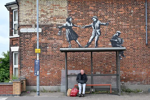 Мужчина ждет автобус на остановке под новым граффити Бэнкси в городе Грейт-Ярмуте на восточном побережье Англии, 8 августа 2021 года.
