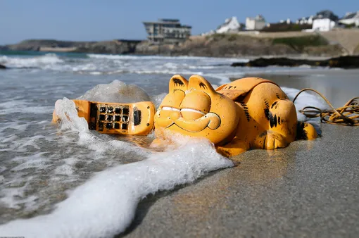 Пластиковый телефон в форме кота Гарфилда найден на берегу пляжа Ле-Конке на западе Франции. Подобные находки в этом районе случаются регулярно на протяжении 30 лет. Теперь этому есть разгадка: выяснилось, что в 1980-х годах во время шторма там затонул транспортировочный контейнер.