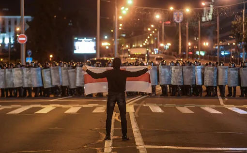 Демонстрант держит флаг перед полицией, вооруженной дубинками и щитами, Минск, Беларусь