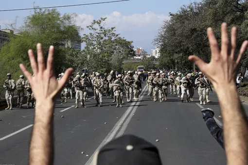 A demonstrator holds up his hands toward advancing soldiers as a state of emergency remains in effect in Santiago, Chile, Sunday, Oct. 20, 2019. Protests in the country have spilled over into a new day, even after President Sebastian Pinera cancelled the subway fare hike that prompted massive and violent demonstrations