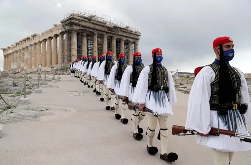 25 марта 2021 года, солдаты президентской гвардии проходят перед храмом Парфенон на вершине Акрополя после церемонии поднятия греческого флага в Афинах. Греция отмечает двухсотлетие начала войны за независимость против Османской империи