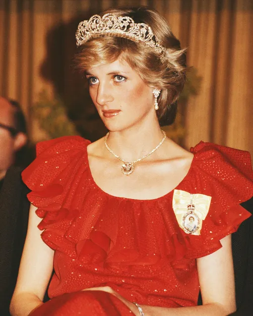 Diana, Princess of Wales (1961 — 1997) wearing a red Bruce Oldfield gown to a state reception at the Wrest Point Federal hotel in Hobart, Tasmania, 30th March 1983. She is wearing the Spencer family tiara and the badge of the Royal Family Order of Elizabeth II, and has restyled the Prince of Wales feathers brooch as a necklace. Her pearl and diamond earrings were a gift from the Emir of Qatar. (Photo by Tim Graham Photo Library via Getty Images)