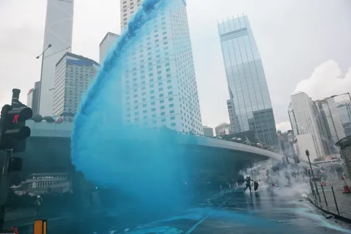 A protestor throws back an exploded tear gas shell, as police fire blue-colored water from water cannons in central Hong Kong, Saturday, Aug. 31, 2019. While other protesters marched back and forth elsewhere in the city, a large crowd wearing helmets and gas masks gathered outside the city government building. Some approached barriers that had been set up to keep protesters away and appeared to throw objects at the police on the other side. Others shone laser lights at the officers.