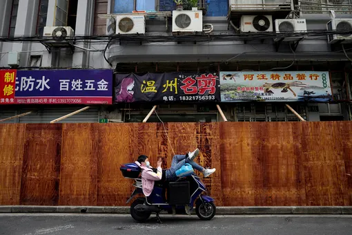 A man uses a mobile phone while leaning on a scooter in front of barricades of a sealed-off area, following the coronavirus disease (COVID-19) outbreak in Shanghai, China March 30, 2022. REUTERS/Aly Song