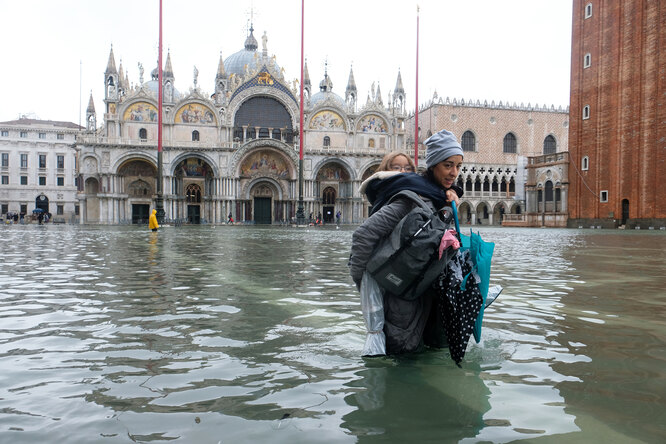 Женщина с ребенком пытаются пройти через затопленную площадь Святого Марка