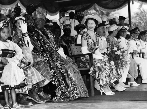 1956: Travelling and representing BфОфициальные визиты в страны Содружества были одной из важнейших функций Елизаветы II.ritain overseas is a key part of her job. She and her husband, Prince Philip, visited the Lagos City boundary in Nigeria on their way to the city from Ikeja Airport in 1956. Here, she's sat next to Chief Oba Adeniji-Adila II, whose family has ruled in Lagos for 260 years.