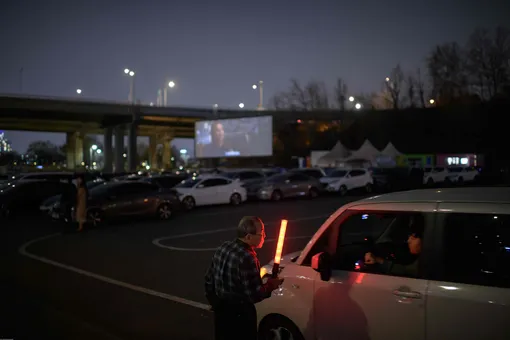 Билетер руководит движением на парковке drive-in кинотеатра в Сеуле.