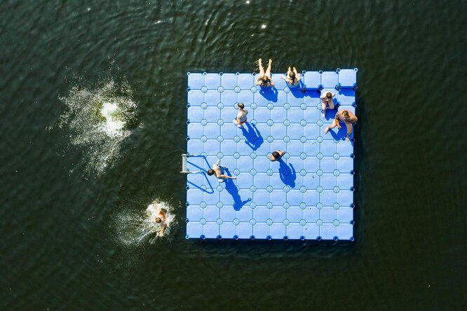 Люди отдыхают на плавающем понтоне на озере Альтвармбюхенер в Ганновере, Германия.