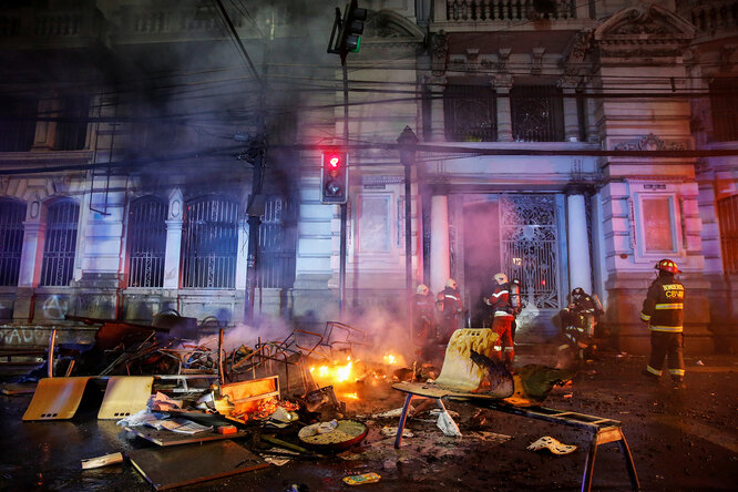 Firemen work near burnt furniture and objects outside the building of Chilean newspaper El Mercurio de Valparaiso during a protest against the government in Valparaiso, Chile