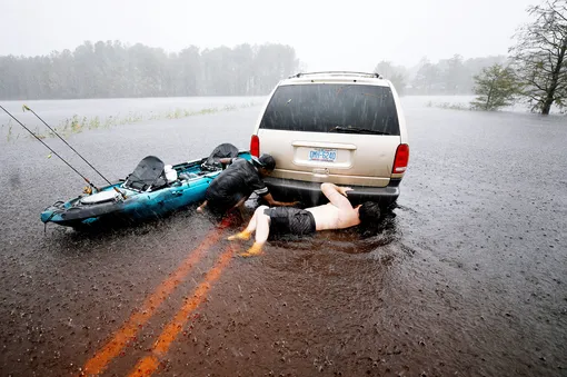 Мужчины пытаются сдвинуть машину, застрявшую на проезжей части из-за ливня, Северная Каролина.