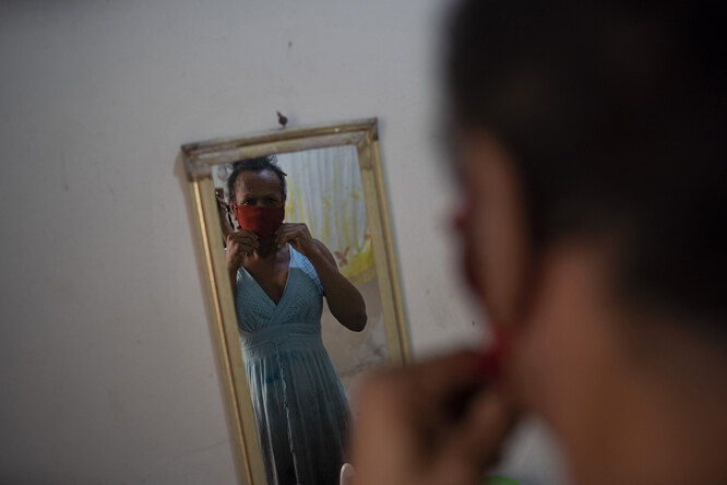 Transgender Claudinha is reflected in a mirror as she puts on a protective face mask inside her room at the squat known as Casa Nem, in Rio de Janeiro, Brazil, Wednesday, July 8, 2020. The six-floor building is home to about 50 LGBTQ people riding out the new coronavirus pandemic behind closed doors.