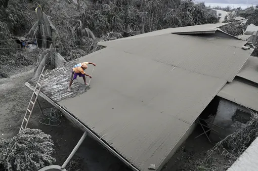 A resident clears volcanic ash from his roof in Laurel, Batangas province, southern Philippines on Tuesday, Jan. 14, 2020. Taal volcano is spewing ash half a mile high and trembling with earthquakes constantly as thousands of people flee villages darkened and blanketed by heavy ash. (AP Photo/Aaron Favila), APTOPIX