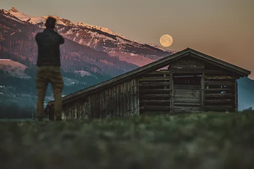 Мужчина фотографирует суперлуние над Альпами из коммуны Пизендорф в Австрии