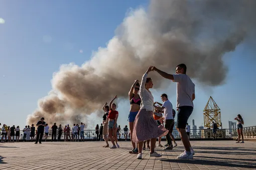 Couples dance samba as smoke rises from a burning pyrotechnics warehouse in Moscow on June 19 2021. (Photo by Couples dance samba as smoke rises from a burning pyrotechnics warehouse in Moscow on June 19 2021. (Photo by Dimitar Dilkoff / AFP / Getty Images)