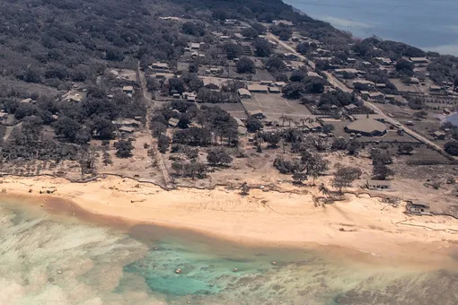 An image taken from a military reconnaissance plane shows a Tongan village inundated with ash, while the beach shows signs of water damage where tsunami waves washed ashore following a huge volcanic eruption at the weekend