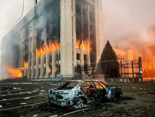 Сгоревший автомобиль возле горящего здания мэрии (акимат). Участники протеста против роста цен на топливо ворвались в здание акимата и пожодгли его. Валерий Шарифулин/ТАСС