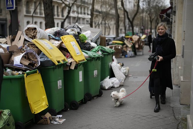 Парижанка выгуливает собаку среди неубранного мусора, 22 марта 2023 года