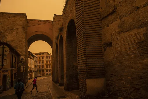 GRANADA, SPAIN — MARCH 15: A woman runs along Calle Elvira as the Saharan Dust colours the sky orange on March 15, 2022 in Granada, Spain. Air masses from Africa often blow a mixture of sand and dust from the Sahara across the Mediterranean sea to Spain. The dust causes high levels of pollution and breathing issues. (Photo by Carlos Gil Andreu/Getty Images)