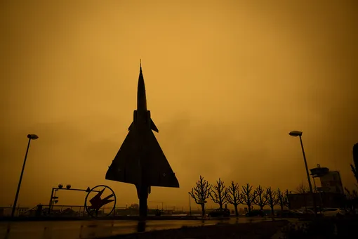 A former Swiss Air Force jet fighter Mirage 2000 manufactured by Dassault Aviation is placed on display in front of the entrance of the Swiss Army at Payerne Air Base as Sahara sand colours the sky in orange and creates a special light atmosphere, Switzerland, Tuesday, March 15, 2022. A huge dust storm is swirling over Europe from the Sahara desert. (Laurent Gillieron/Keystone via AP), APTOPIX