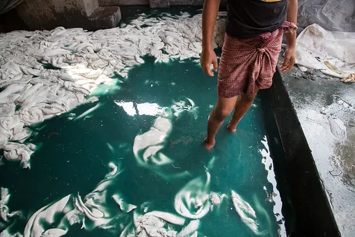 На текстильной фабрике в в Дакке, Бангладеш, работник обрабатывает ткань химикатами, не имея специальной одежды и средств защиты
