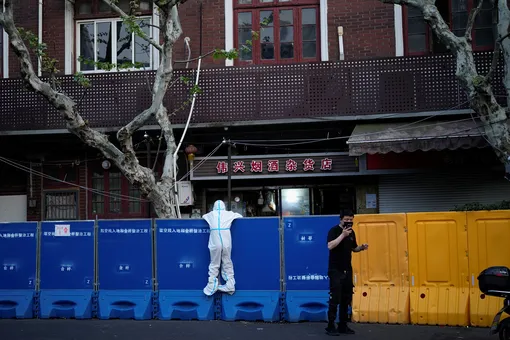 A person in a protective suit looks over barricades set around a sealed-off area, during a lockdown to curb the spread of the coronavirus disease (COVID-19) in Shanghai, China April 11, 2022. REUTERS/Aly Song