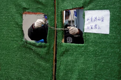 A security guard wearing protective gear sets up barriers from inside a sealed-off area, before the second stage of a two-stage lockdown to curb the spread of the coronavirus disease (COVID-19), in Shanghai, China March 31, 2022. REUTERS/Aly Song