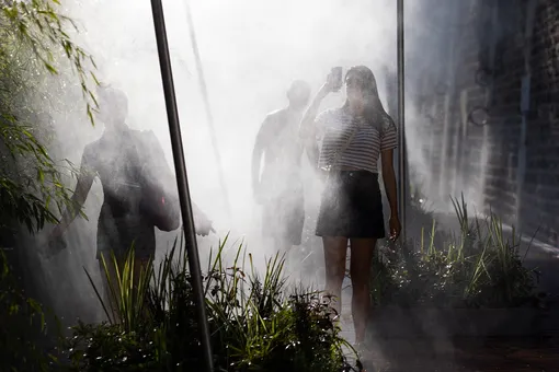 Люди наслаждаются водяным туманом на набережной Сены во время аномальной жары в Париже.