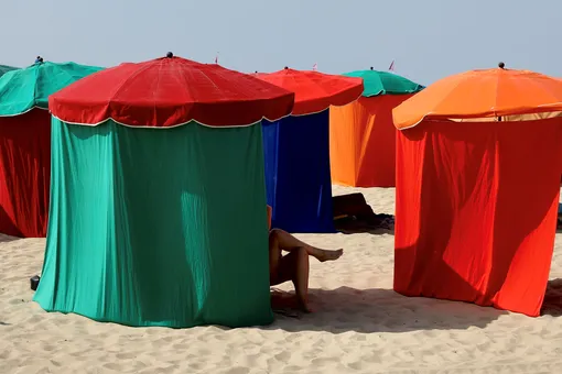 Женщина отдыхает под тентом на пляже в Довиле.