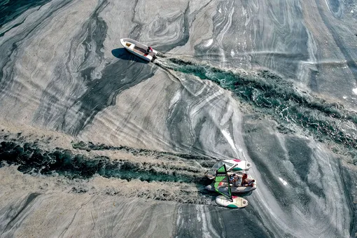 This aerial photograph taken on June 8, 2021 on the Caddebostan shore of Turkey's Marmara Sea, shows a boat sailing among mucilage, a jelly-like layer of slime that develops on the surface of the water due to the excessive proliferation of phytoplankton, gravely threatening the marine biome. — The mucilage has been informally referred to as «sea snot» and was first documented in Turkey's waters in 2007. Experts warn the mucilage will occur more often because of global warming. (Photo by )