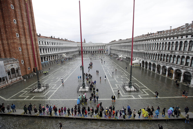 Люди идут по специально установленному подиуму на затопленной площади Святого Марка
