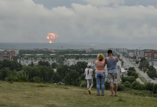 In this photo taken on Monday, Aug. 5, 2019, a family watches explosions at a military ammunition depot near the city of Achinsk in eastern Siberia's Krasnoyarsk region, in Achinsk, Russia. Russian officials say powerful explosions at a military depot in Siberia left 12 people injured and one missing and forced over 16,500 people to leave their homes.