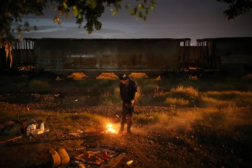 A drug addict warms himself at a trash fire, in the waste ground next to the Malverde shrine