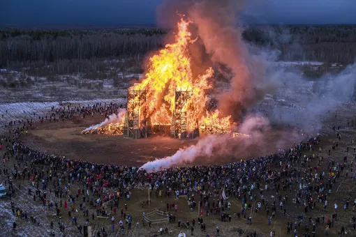 Люди наблюдают, как горит инсталляция, изображающая мост, в рамках празднования Масленицы в парке художников Никола-Ленивец недалеко от Москвы. Снимок сделан 29 февраля 2020