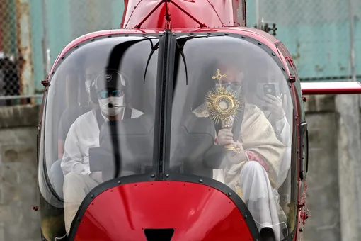 Викарный Епископ Джованни Баттиста Пичолли (справа) в защитной маске дает свое благословение эквадорскому городу Гуаякиль, пролетая над ним во время Страстной недели. 9 апреля 2020