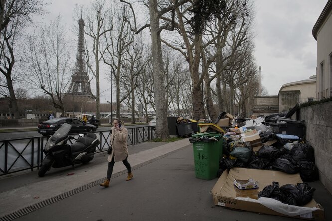 Женщина проходит мимо неубранного мусора в Париже. Французские сборщики мусора, рабочие НПЗ и другие муниципальные служащие бастуют. Президент Франции Эммануэль Макрон заявил, что пенсионный законопроект, принятый без голосования в парламенте, должен быть реализован к концу года