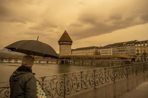 The Kapellbruecke (literally, Chapel Bridge) and the Wasserturm (Water Tower) in Lucerne appear in new colours, as Sahara sand colours the sky in orange and creates a special light atmosphere, Switzerland, Tuesday, March 15, 2022. (Urs Flueeler/Keystone via AP)