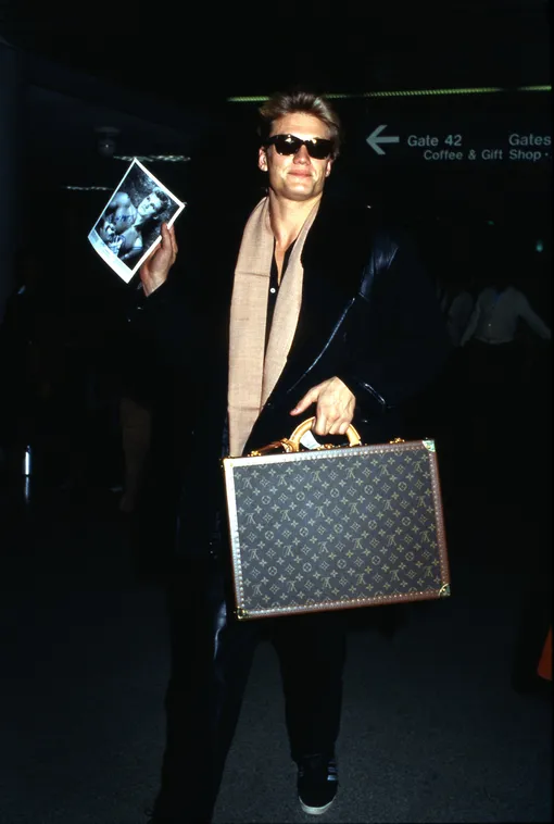 LOS ANGELES — 1986: Actor Dolph Lundgren holds an autographed photo of himself and a Louis Vitton suitcase at LAX airport in 1986 in Los Angeles, California. (Photo by )